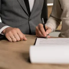 Dwie osoby przy biurku podpisują dokument. Jedna z nich wypełnia wniosek o niekaralności online.