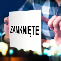 Osoba przykleja kartkę z napisem "ZAMKNIĘTE" na szybę, co może symbolizować decyzję o tym, jak zamknąć działalność gospodarczą.