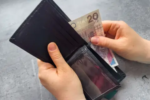 Dłonie wkładają banknot 20 zł do portfela. Zastanawiasz się, po jakim czasie od zarejestrowania wypłacany jest zasiłek dla bezrobotnych?