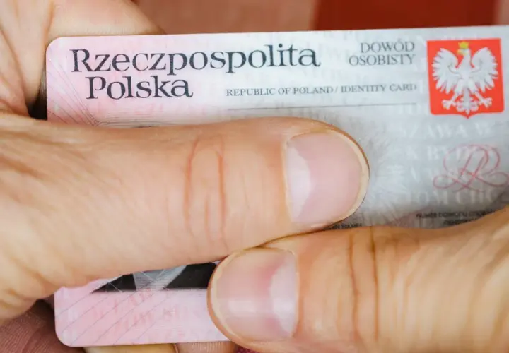 Dłonie trzymają polski dowód osobisty. Widoczna jest seria i numer dowodu, godło Polski oraz napisy "Rzeczpospolita Polska" i "Dowód osobisty".