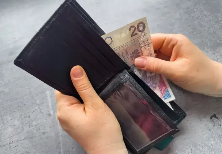 Dłonie wkładają banknot 20 zł do portfela. Zastanawiasz się, po jakim czasie od zarejestrowania wypłacany jest zasiłek dla bezrobotnych?