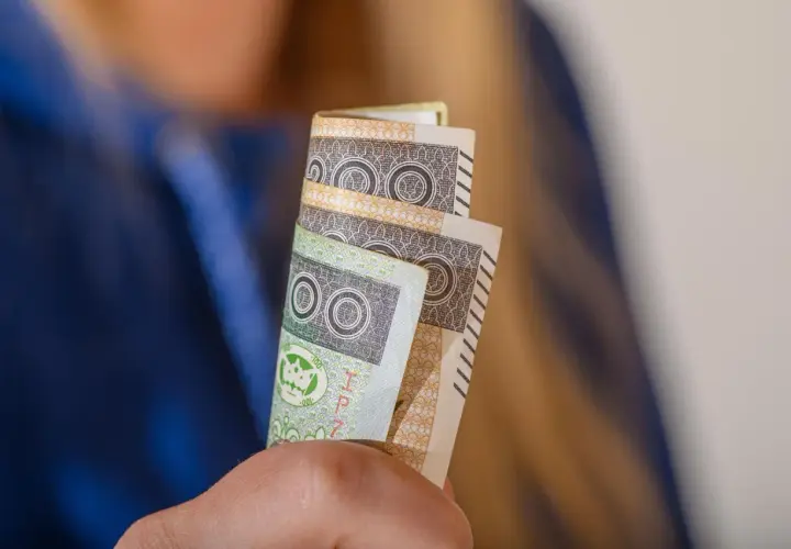 Orzeczenie o niepełnosprawności to podstawa do ubiegania się o zasiłek pielęgnacyjny. Dłonie trzymają banknoty 100 zł.