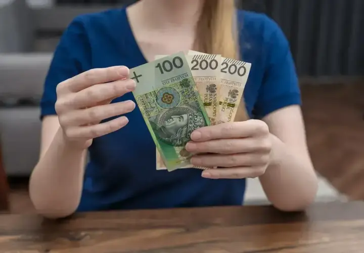 Kobieta trzyma banknot 100 zł i dwa po 200 zł. Łącznie 500 zł, czyli połowa kwoty 1000 plus.
