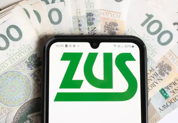 Telefon z logo ZUS na tle banknotów 100 zł. Dowiedz się, komu przysługuje dodatek pielęgnacyjny z ZUS.