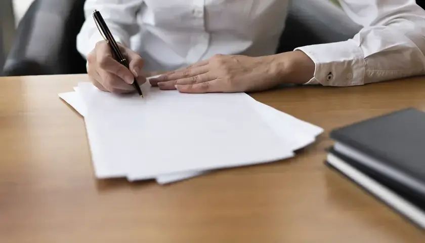 Dłoń pisze długopisem na białej kartce. Obok leżą notatniki. Szybka parafka i do dzieła!
