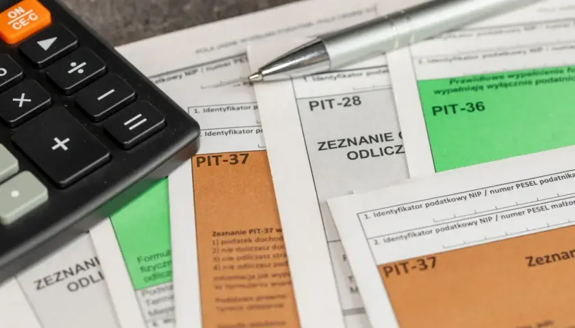 Kalkulator i długopis leżą na dokumentach podatkowych, w tym na formularzu PIT-28.