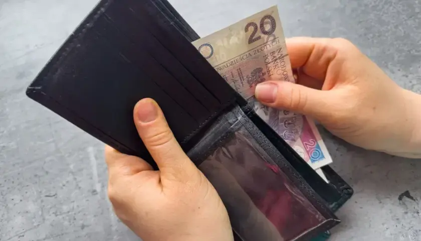 Dłonie wkładają banknot 20 zł do portfela. Zastanawiasz się, po jakim czasie od zarejestrowania wypłacany jest zasiłek dla bezrobotnych?
