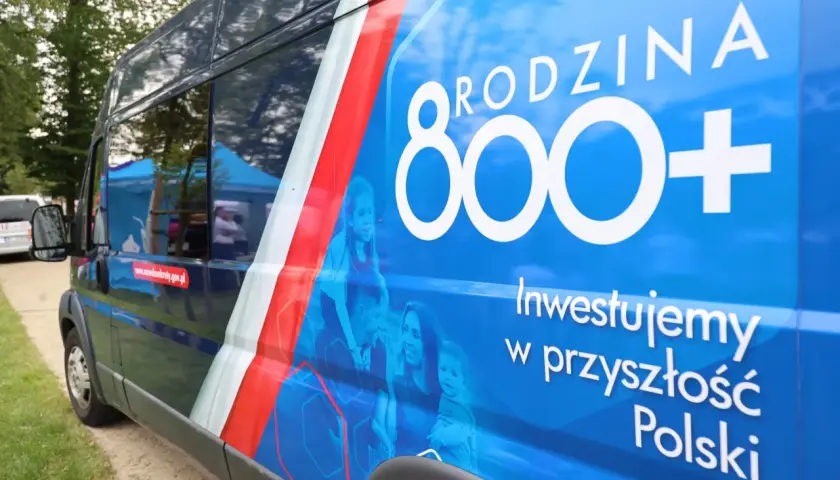 Niebieski bus z napisem "RODZINA 800+" i hasłem "Inwestujemy w przyszłość Polski". Obok rodziny, symbolizującej program 800 plus zmiany.