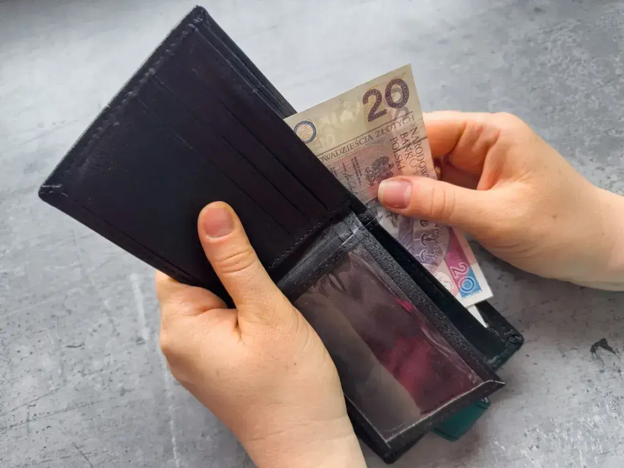 Dłonie wkładają banknot 20 zł do portfela. Zastanawiasz się, po jakim czasie od zarejestrowania wypłacany jest zasiłek dla bezrobotnych?