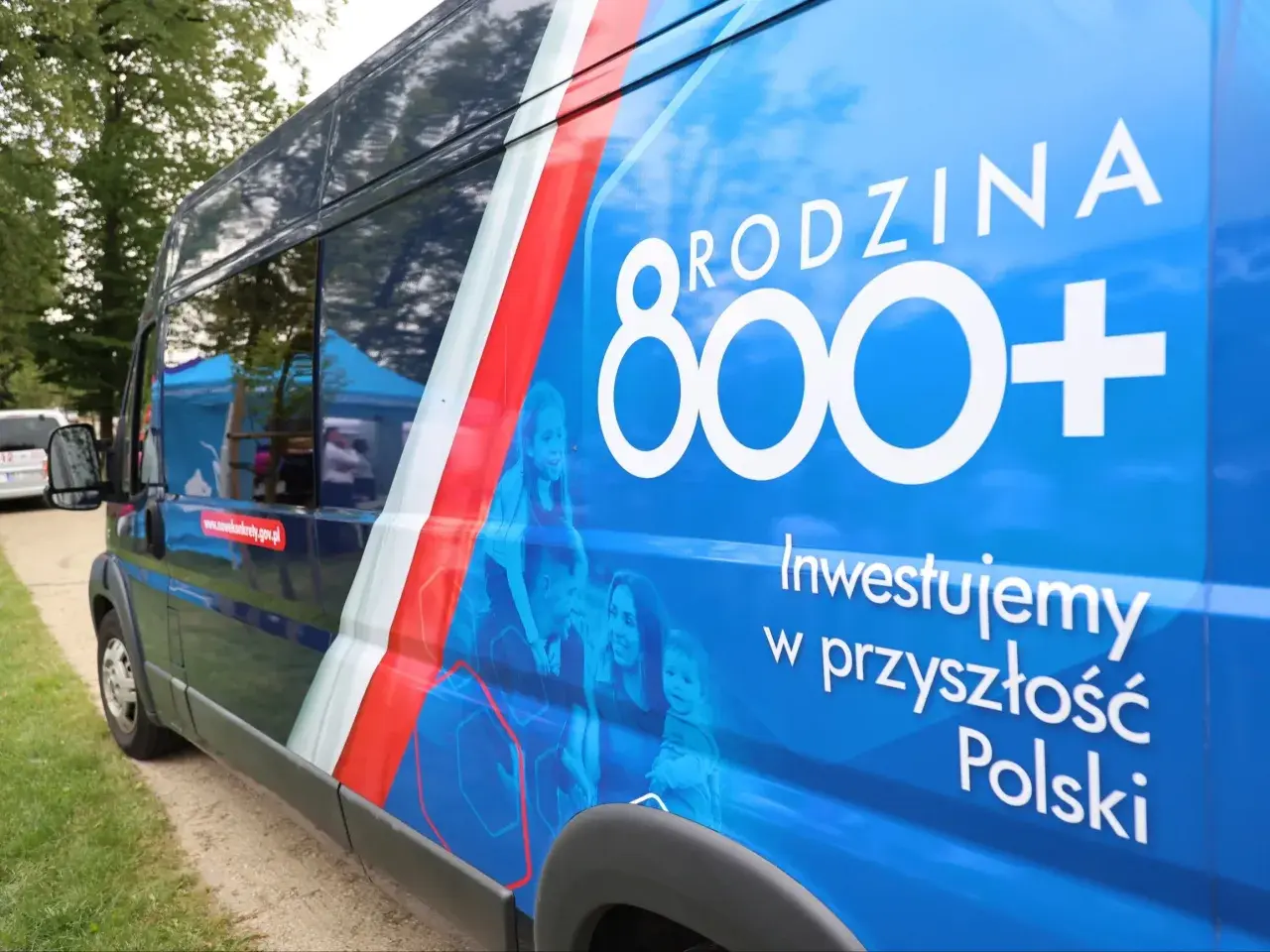 Niebieski bus z napisem "RODZINA 800+" i hasłem "Inwestujemy w przyszłość Polski". Obok rodziny, symbolizującej program 800 plus zmiany.