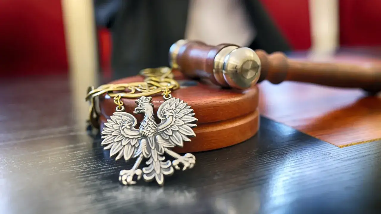 Srebrny orzeł na łańcuszku, młotek sędziowski i drewniana podstawa. Symbolika sprawiedliwości i akwizycji.