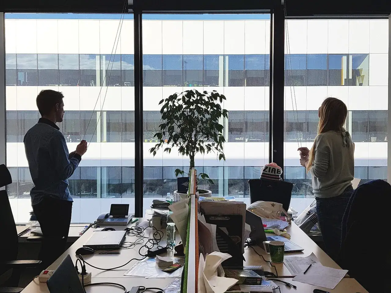 Pracownicy w korporacji co to? Mężczyzna i kobieta przy biurkach, za oknem nowoczesny budynek.